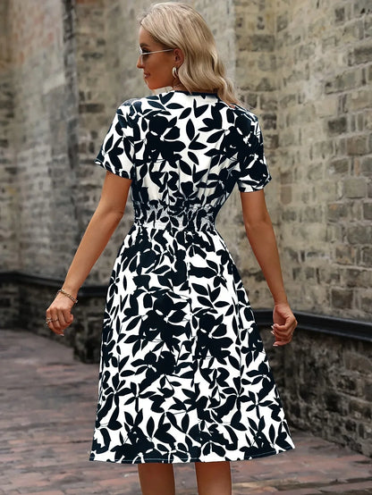 Frau in schwarz-weißem Sommerkleid mit Blattmuster, steht vor einer Steinmauer.