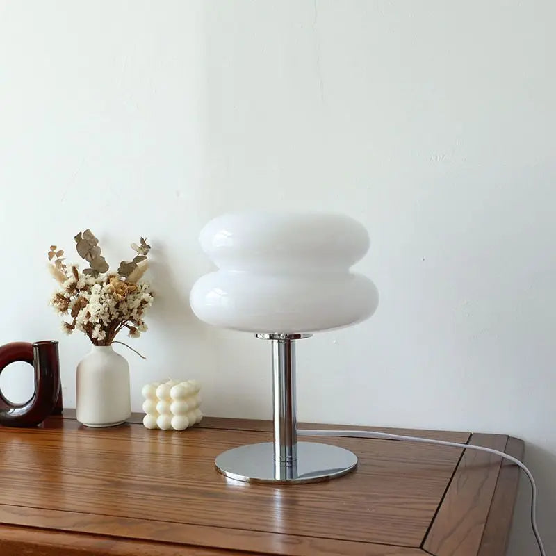 Moderne weiße Tischlampe aus Glas auf Holztisch, dekoriert mit Trockenblumen und Kerze.