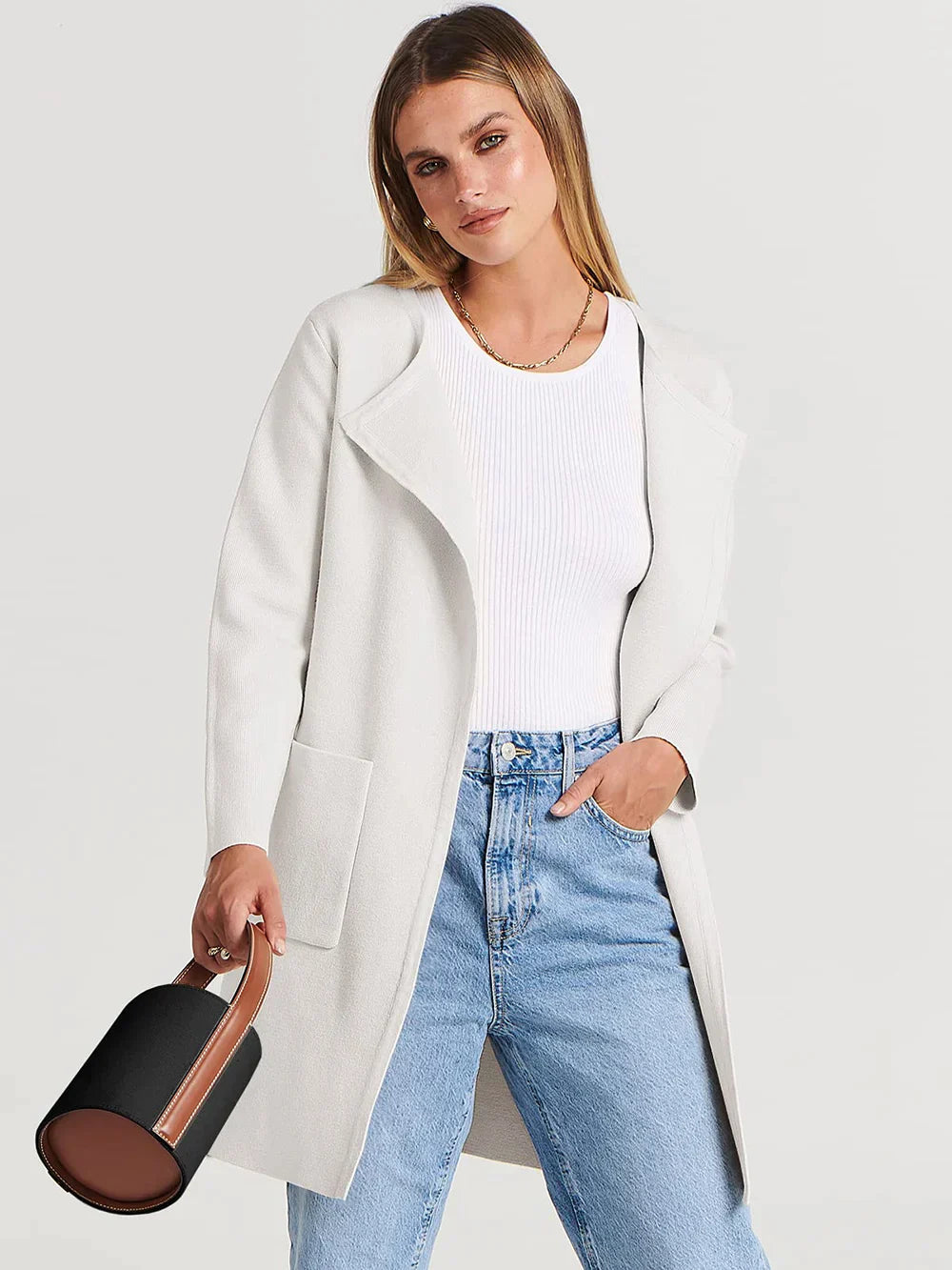 Frau in weißem Mantel, blauer Jeans, weißem Top, hält schwarze Handtasche, Mode, Damenbekleidung.