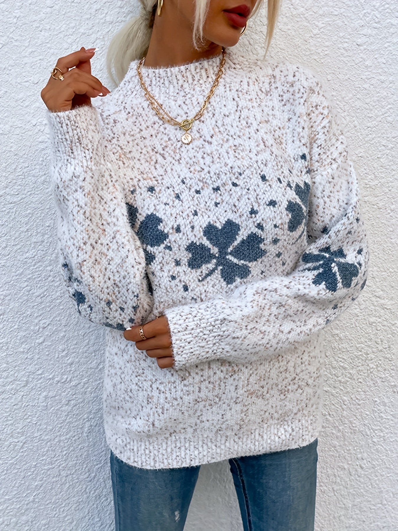 Frau trägt weißen Strickpullover mit grauem Blumenmuster, goldene Ketten, lässiger Stil.
