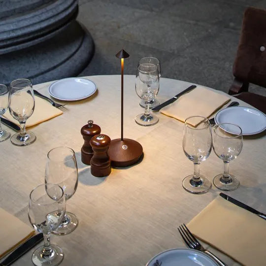 Runder Esstisch mit Tischlampe, Weingläsern, Pfefferstreuer und Servietten in elegantem Ambiente.