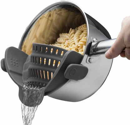 Hand hält Edelstahlkochtopf mit Nudeln, Wasser wird durch schwarzen Silikonsieb abgegossen.