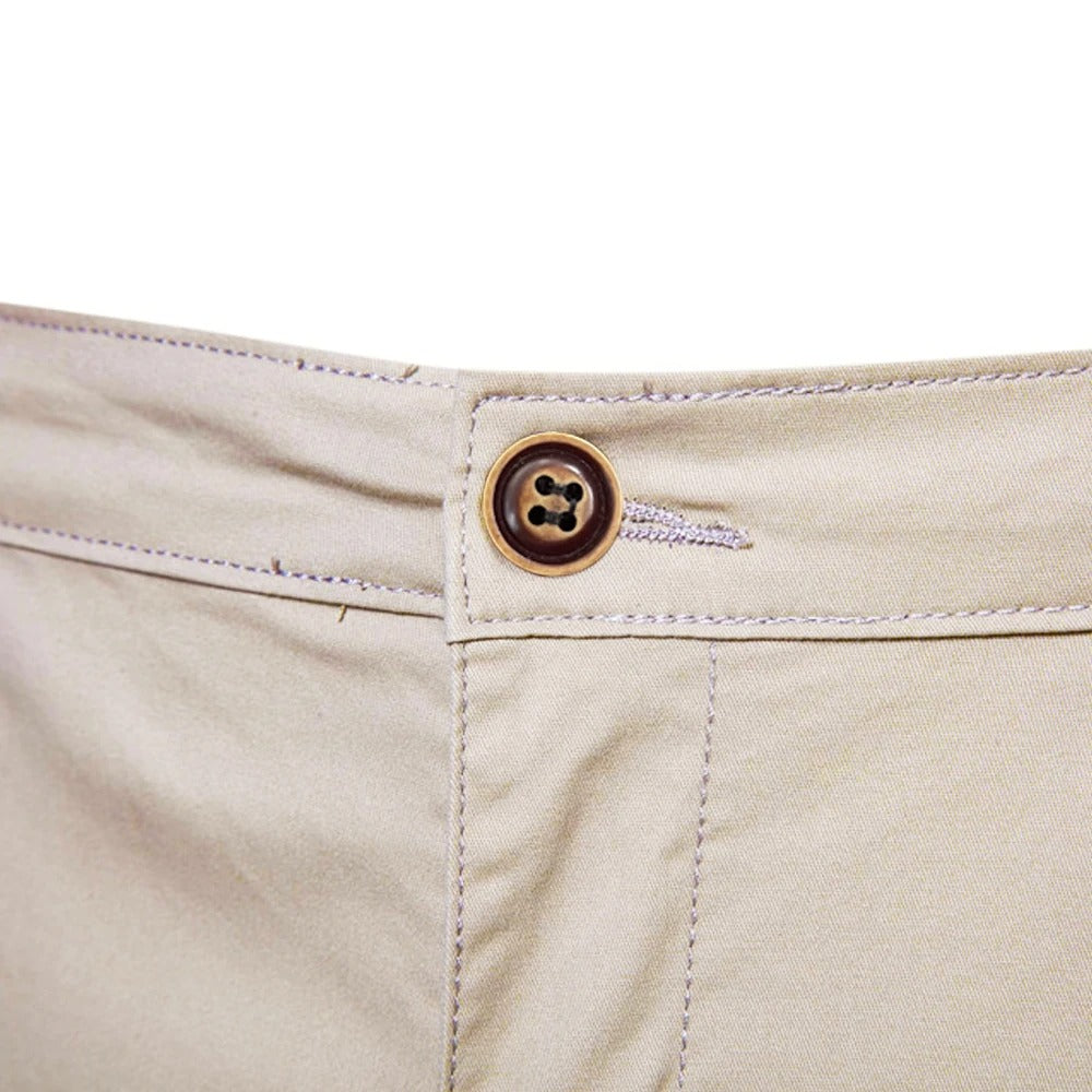 Närbild på midjeknappen i brunt med fyra hål och synliga sömmar på beige shorts. 5