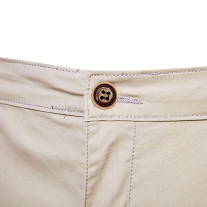 Närbild på midjeknappen i brunt med fyra hål och synliga sömmar på beige shorts. 5
