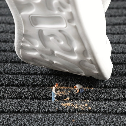 Närbild av mattan där en vit sko trycks mot ytan och miniatyrfigurer fejar bort smuts. 4