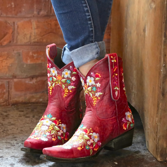 Rote Cowboystiefel mit Blumenstickerei, Damenmode, Leder, lässig, Jeans, rustikaler Hintergrund.