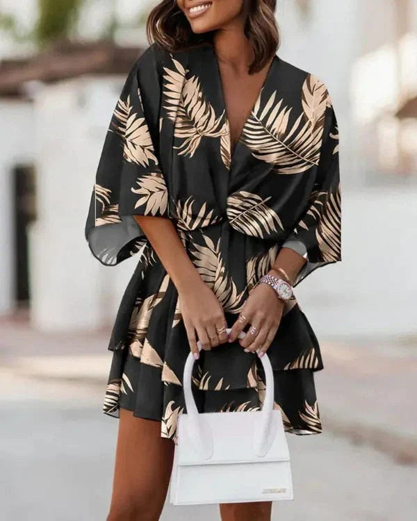 Frau in schwarzem Kleid mit Blattmuster, trägt weiße Handtasche, modisch, elegant, Sommermode.