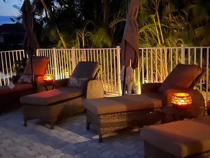 Rattan-Liegen mit Kissen und Laternen auf Terrasse bei Dämmerung, gemütliche Outdoor-Möbel.