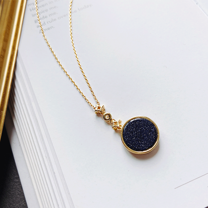 Goldene Halskette mit rundem, blauem Anhänger auf offenem Buch, elegantes Schmuckdesign.