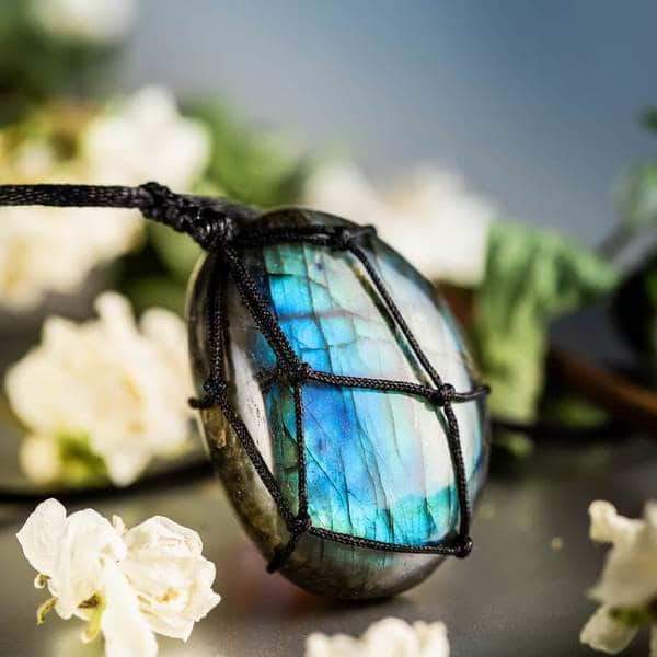 Labradorit-Anhänger mit schwarzem Band, umgeben von weißen Blüten, Schmuck, Edelstein, Geschenk.