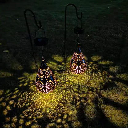 Zwei hängende Solarlaternen, tropfenförmig, mit Blumenmuster, beleuchten Rasen bei Nacht.