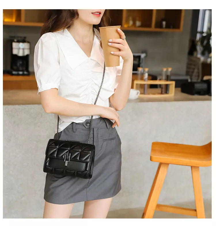 Frau mit weißer Bluse, grauem Rock, schwarzer Umhängetasche, hält Kaffeebecher in Café.