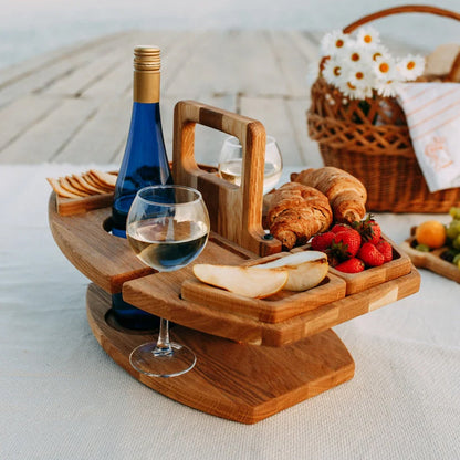 Holz-Picknicktisch mit Weinflasche, Gläsern, Brot, Erdbeeren und Käse auf Decke am Strand.
