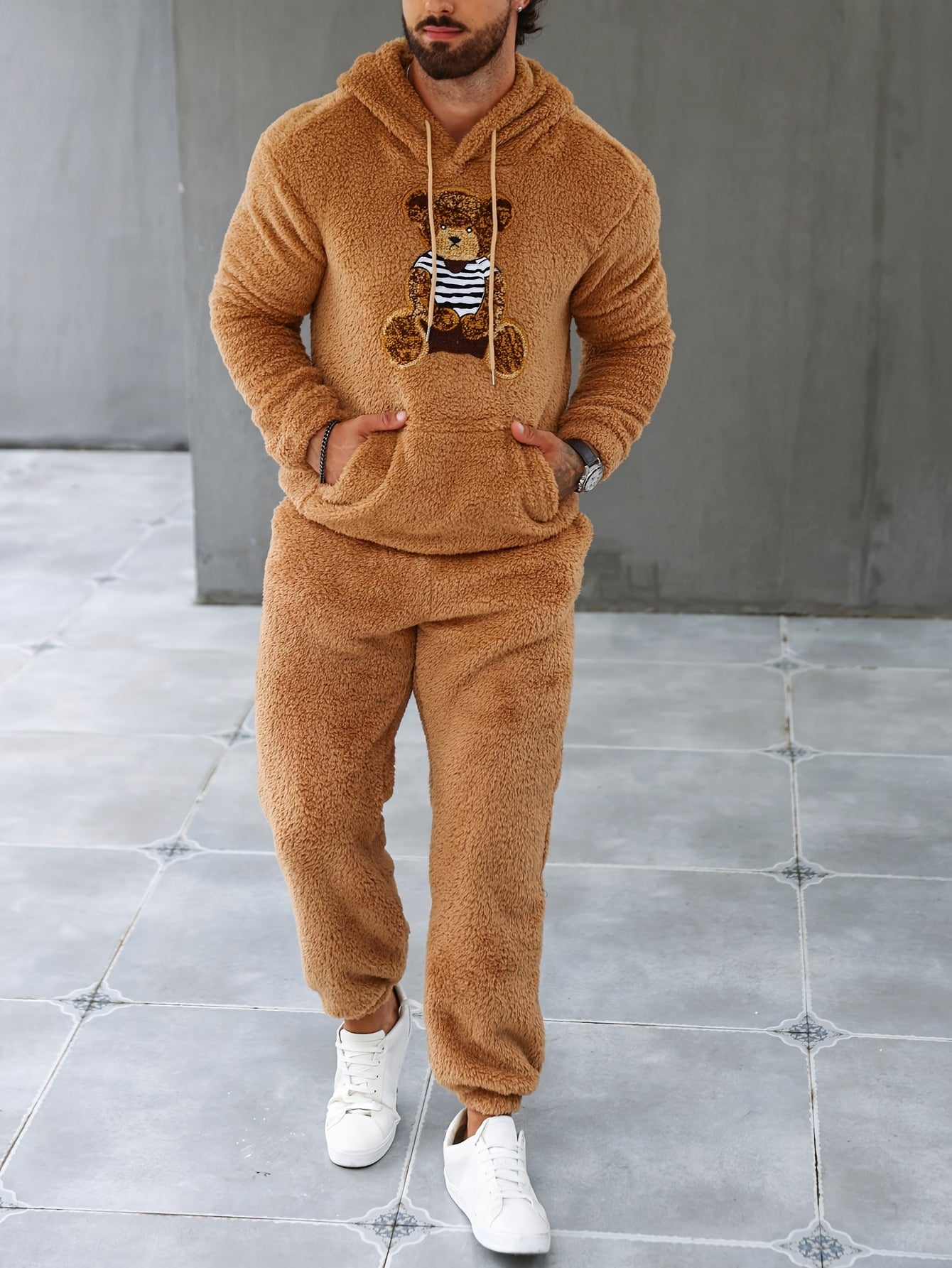 Mann in braunem Teddyfleece-Trainingsanzug mit Bärenmotiv, weiße Sneaker, modisch, gemütlich.
