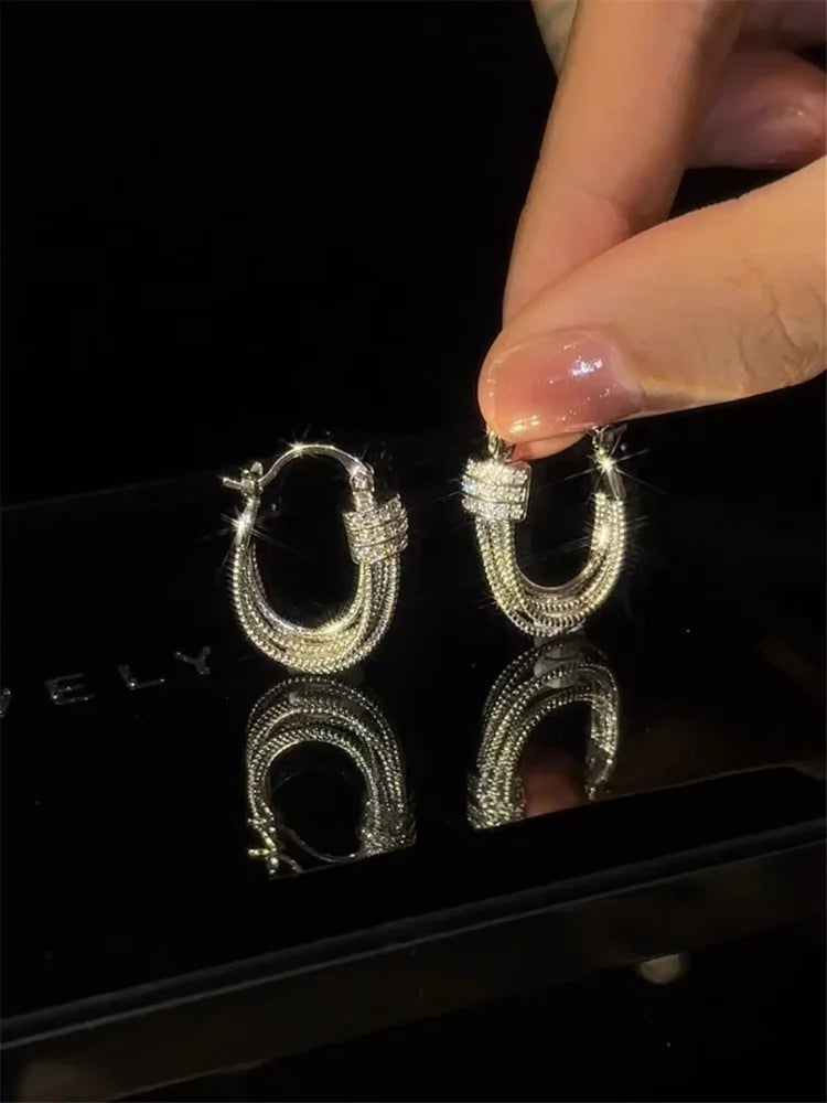 Silberne Creolen-Ohrringe mit Strasssteinen, glänzend, eleganter Schmuck, Hand hält Ohrring.