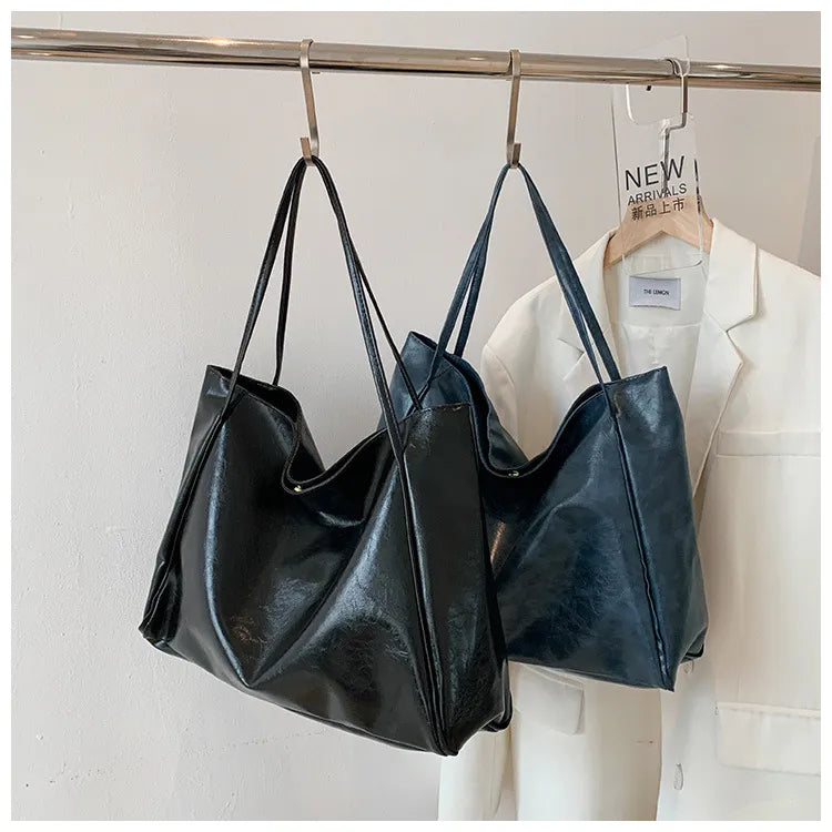Zwei große Ledertaschen in Schwarz und Blau, hängend an Kleiderstange, modisch und elegant.