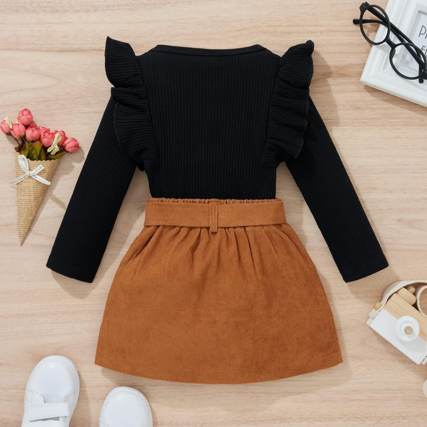 Schwarzes Langarm-Kleid mit Rüschen, brauner Rock, Kinderkleidung, Herbstmode, flach gelegt.