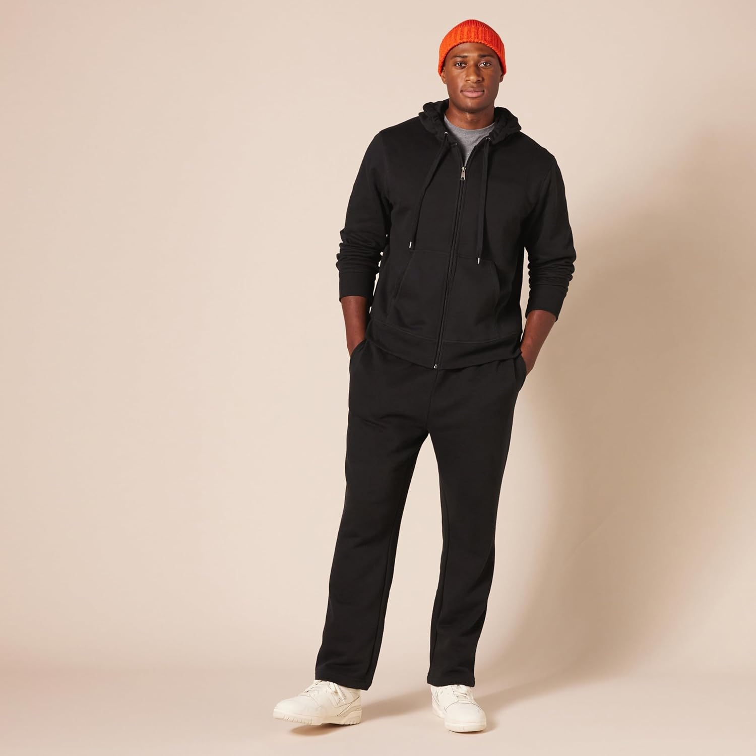 Mann in schwarzem Hoodie und Jogginghose, orange Mütze, weiße Sneaker, lässige Mode.