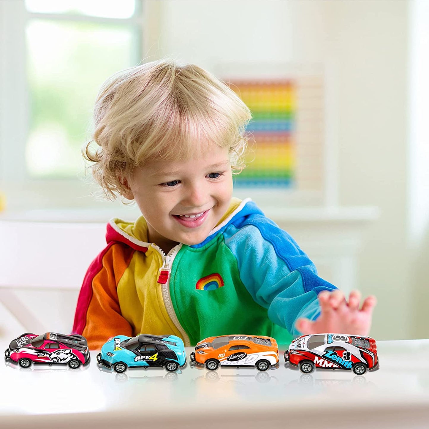 Kleinkind spielt mit bunten Spielzeugautos auf Tisch, Regenbogenjacke, fröhliches Lächeln.