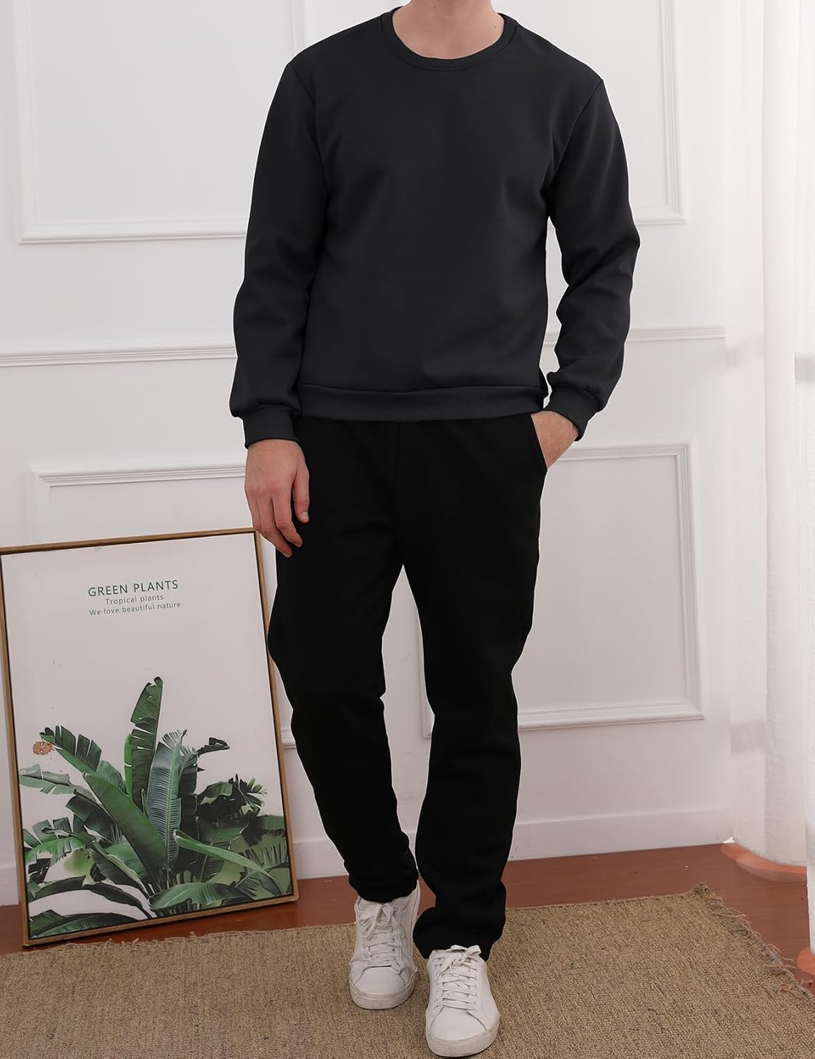 Mann in schwarzem Sweatshirt und Jogginghose, weiße Sneaker, modernes Wohnzimmer.