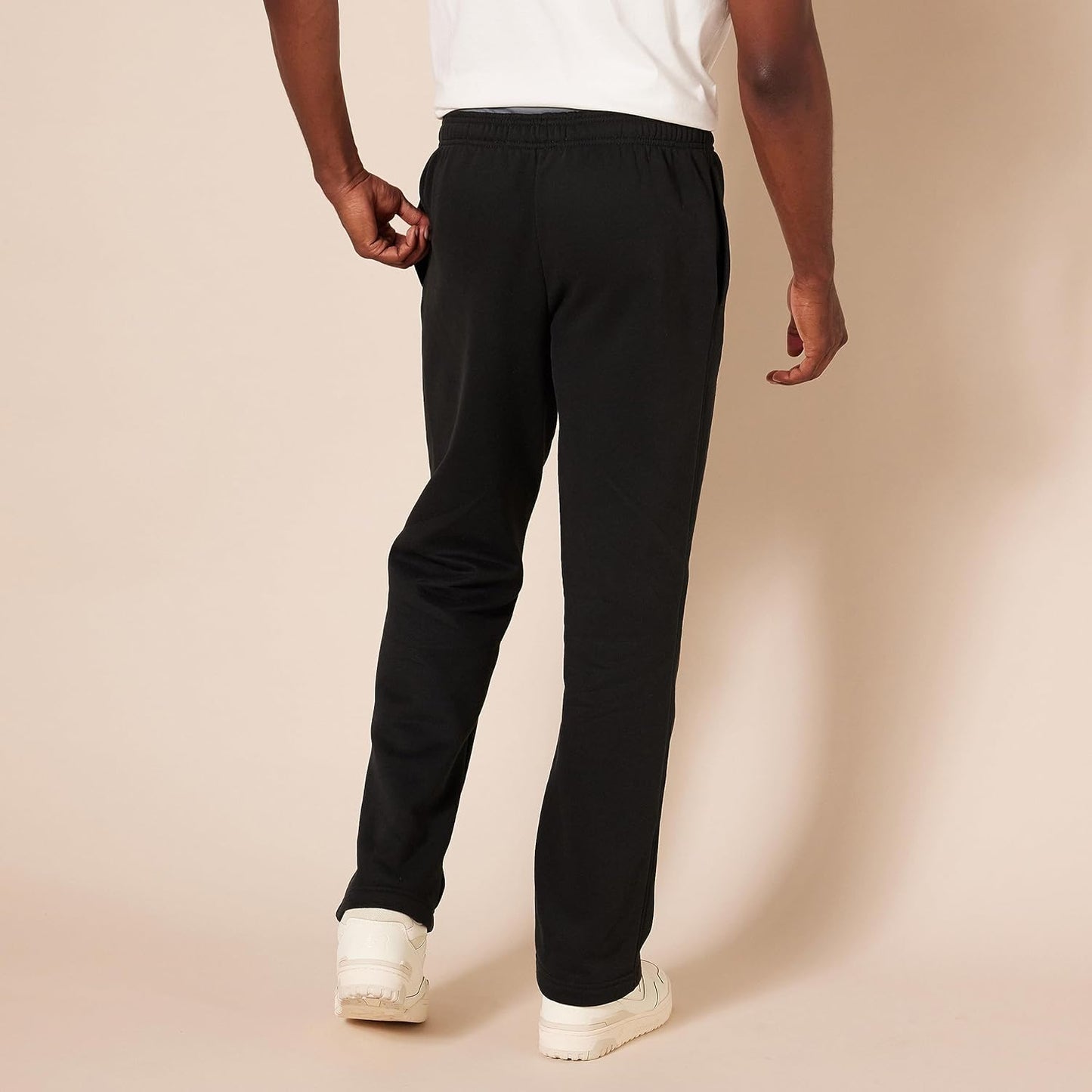 Mann in schwarzer Jogginghose, Rückansicht, weißes T-Shirt, Freizeitmode, beiger Hintergrund.