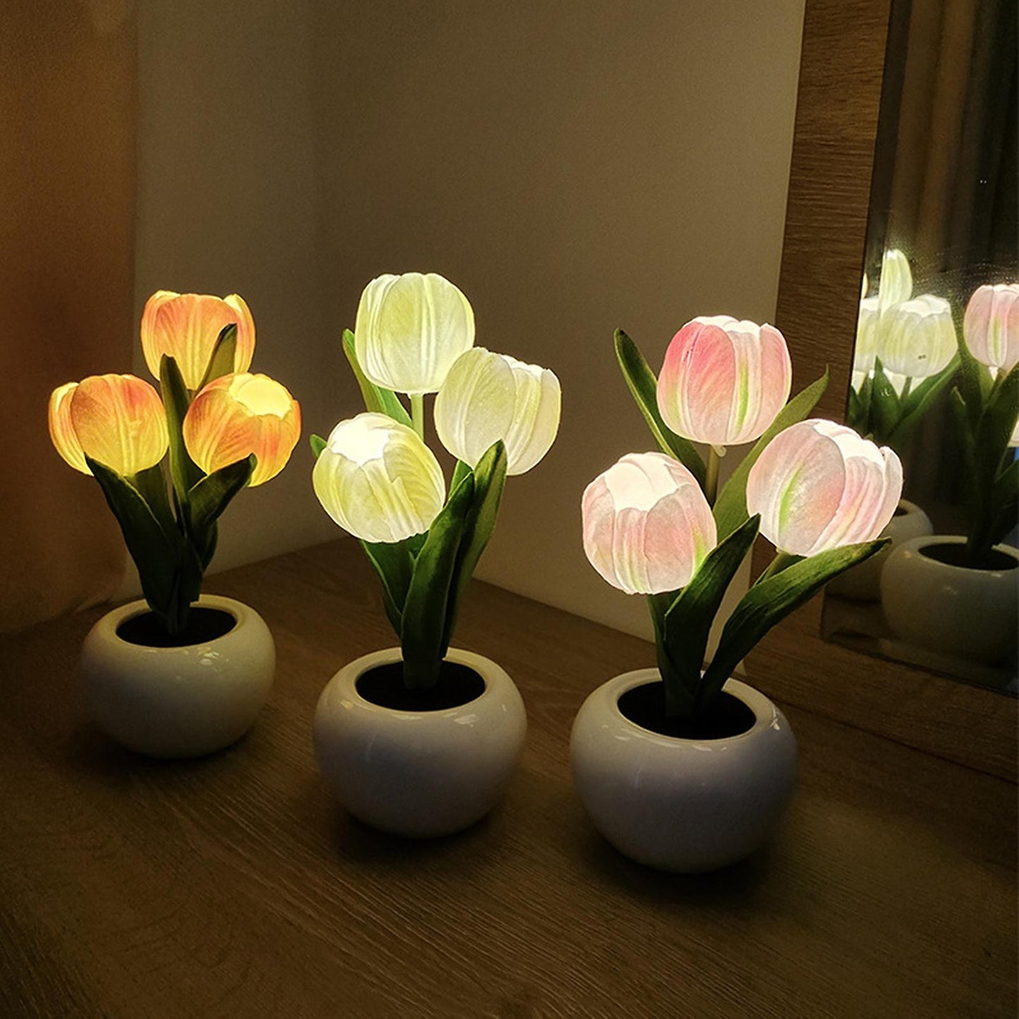 Drei LED-Tulpenlampen in weißen Töpfen auf Holzoberfläche, leuchtend in verschiedenen Farben.