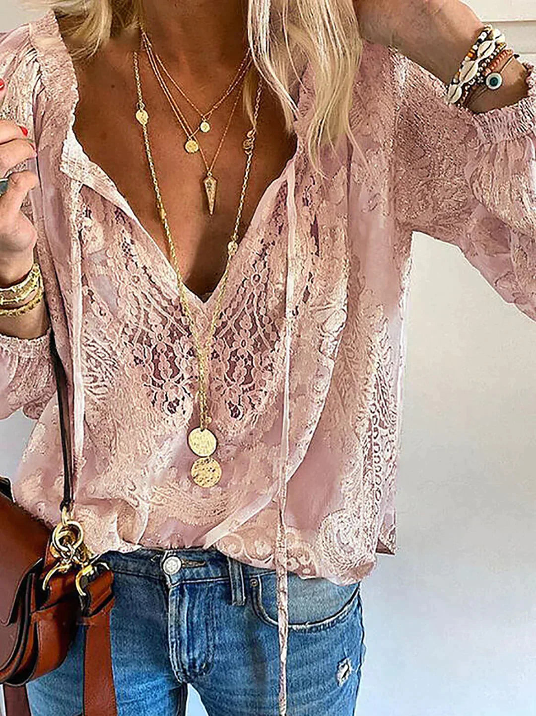 Frau in rosa Spitzenbluse, Jeans und Schmuck, modisches Outfit, lässiger Stil.