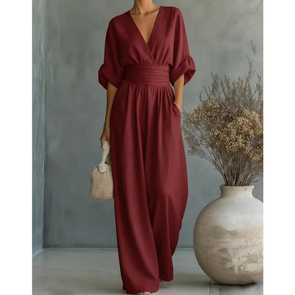 Närbild framifrån av den vinröda jumpsuiten med V-ringning, bred midja och vida byxben mot grå bakgrund. 8