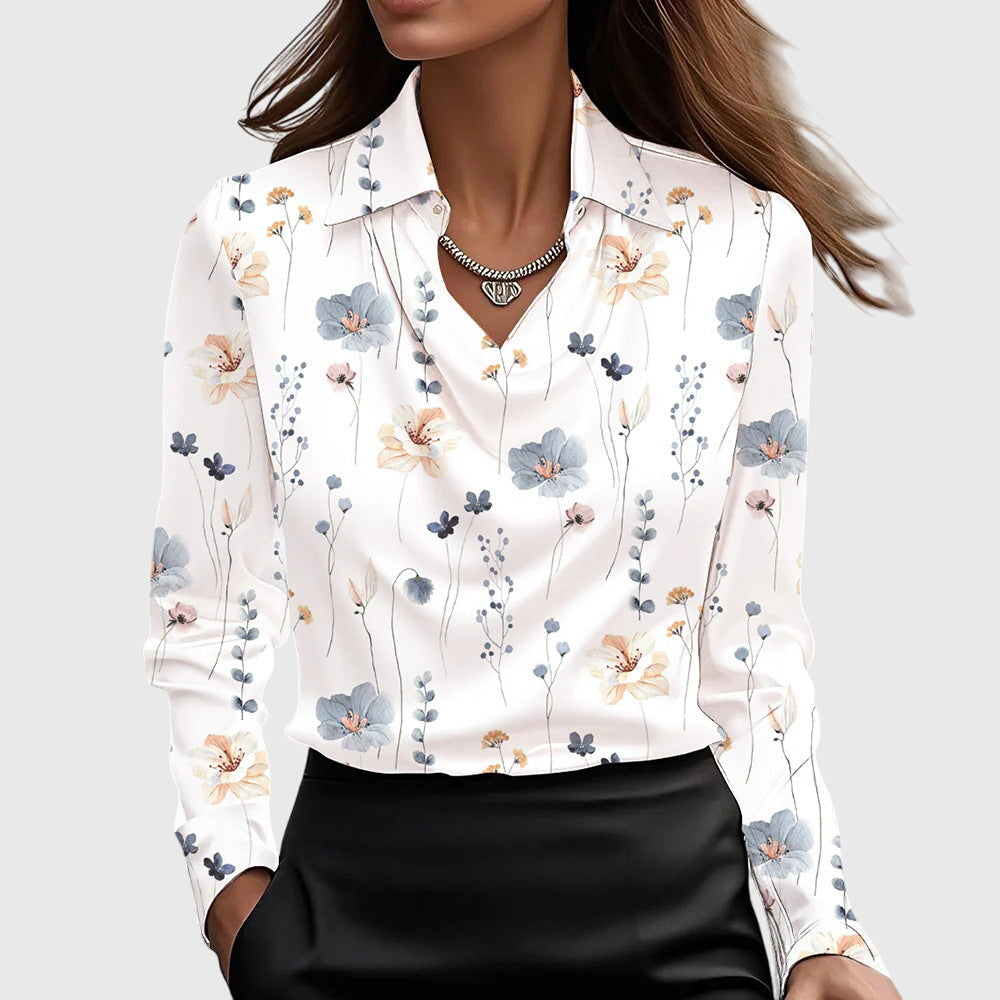 Modell bär vit blus med små blå, persikofärgade och rosa blommor över hela plagget, draperad hals och svart kjol. 9