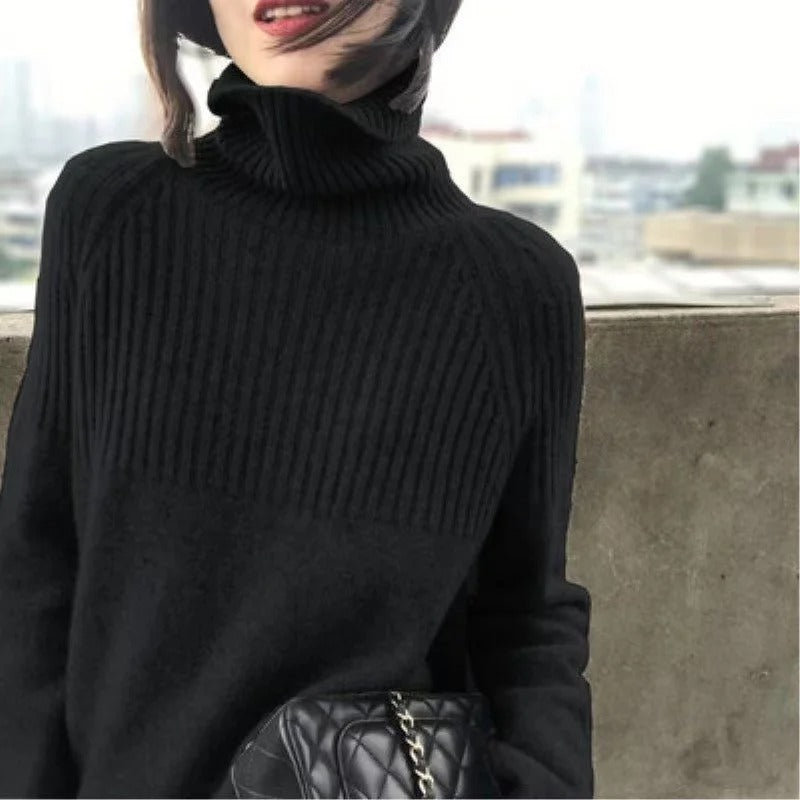 Frau in schwarzem Rollkragenpullover mit schwarzer gesteppter Handtasche, Stadt im Hintergrund.