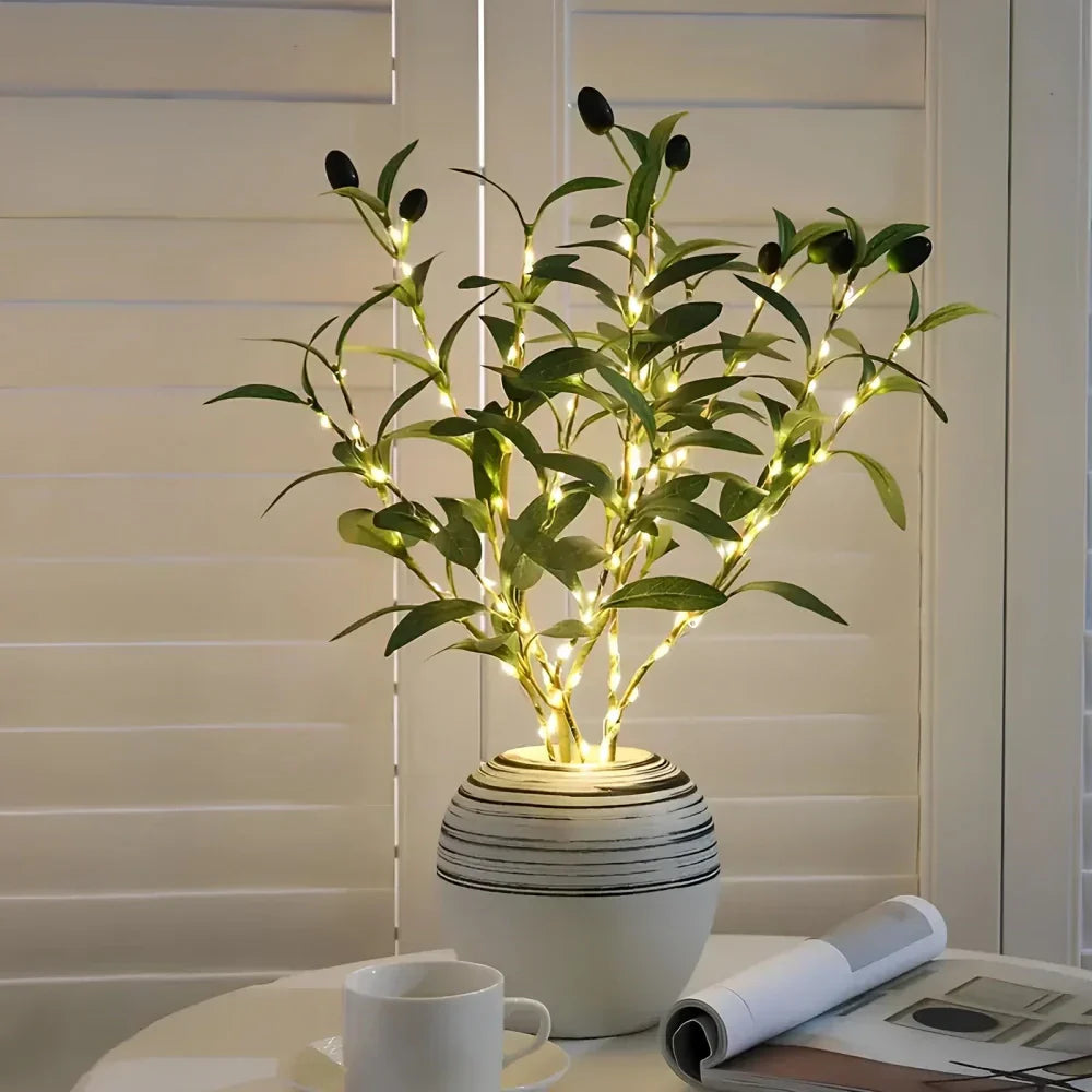 Künstlicher Olivenbaum mit LED-Lichtern in weißem Keramiktopf auf Tisch, moderne Dekoration.