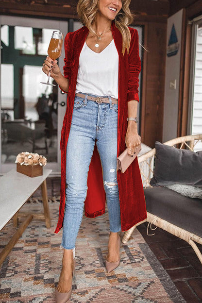 Frau in rotem Samt-Cardigan, blauer Jeans, hält Weinglas, modisch, lässig, Wohnzimmer.