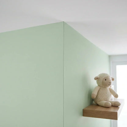 Hörn mellan grönmålade väggar och vitt tak, med en stickad lammgosedjur på en hylla 5