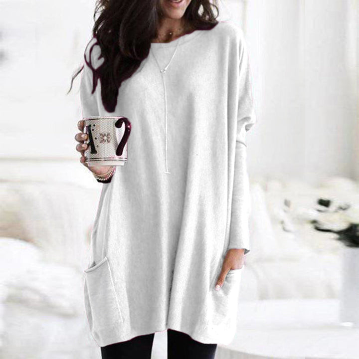 Frau in weißem Oversize-Pullover mit Tasse, gemütliche Wintermode, Wohnzimmer.