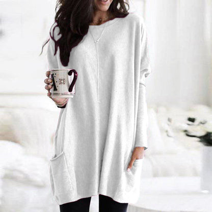 Frau in weißem Oversize-Pullover mit Tasse, gemütliche Wintermode, Wohnzimmer.