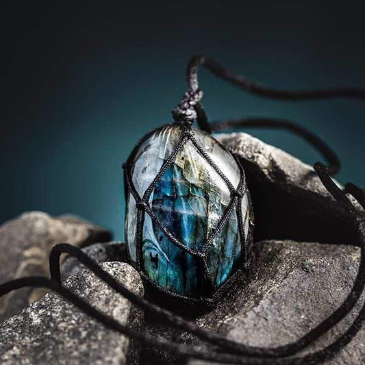 Labradorit-Anhänger mit schwarzem Band, Edelstein-Schmuck, auf grauem Felsen, Nahaufnahme.