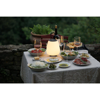 Tisch mit Speisen, Weingläsern und leuchtender Lampe im Freien, Abendessen im Garten.