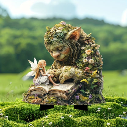 Mossgrön trollfigur som läser i en uppslagen bok med en liten älva på sidan, stående på mossa utomhus. 2