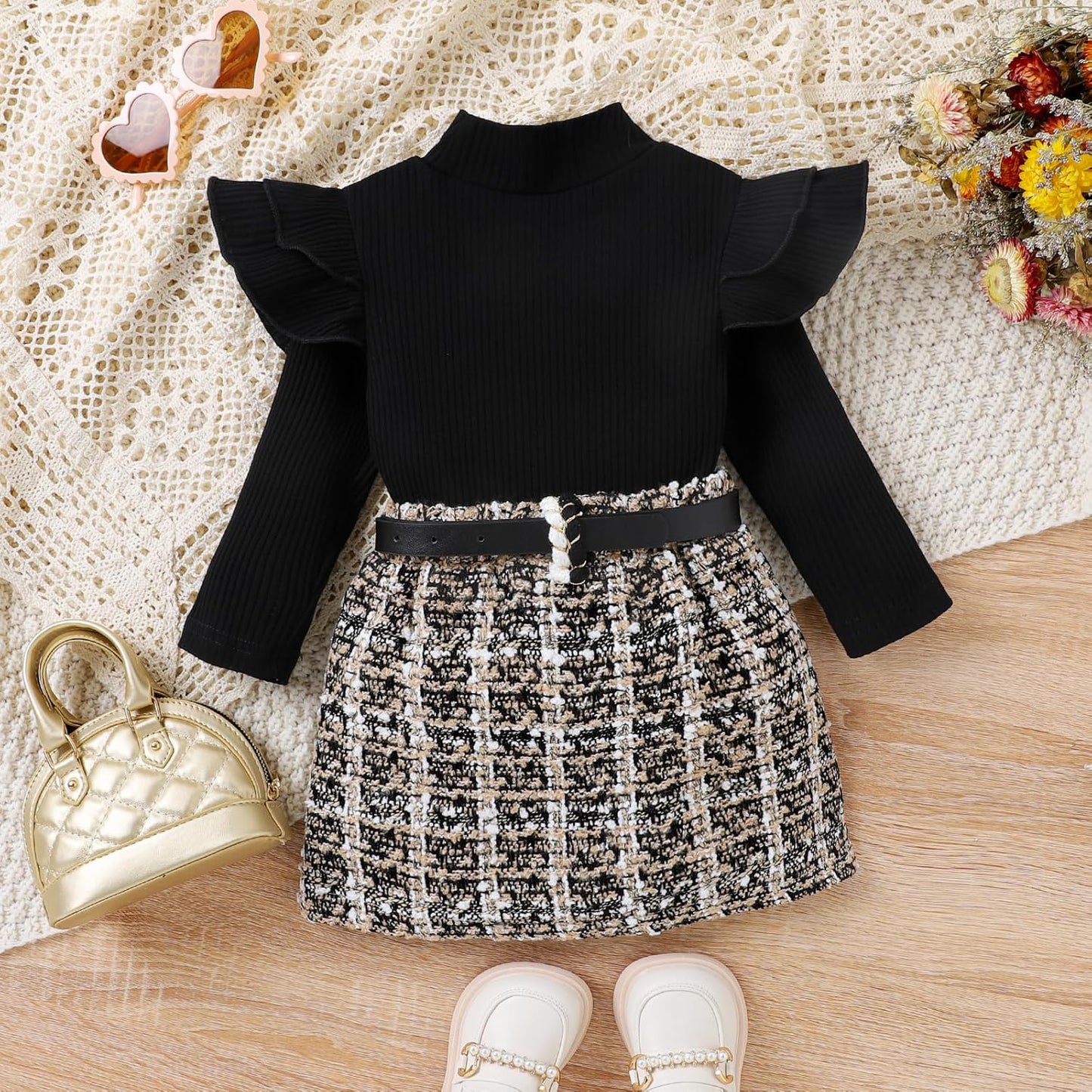 Schwarzes Kinderkleid mit Rüschenärmeln, kariertem Rock und Gürtel auf Holzboden.