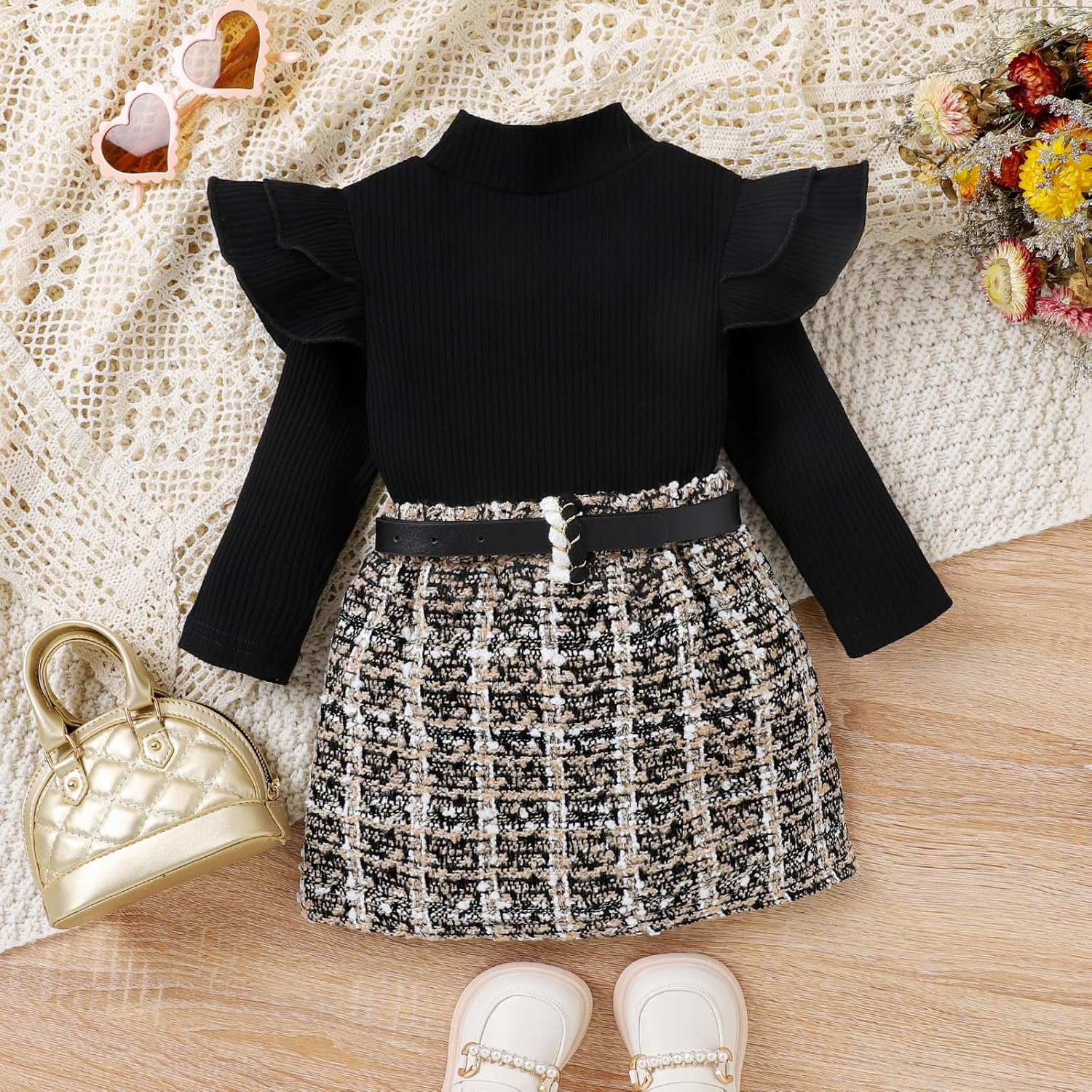 Schwarzes Kinderkleid mit Rüschenärmeln, kariertem Rock und Gürtel auf Holzboden.