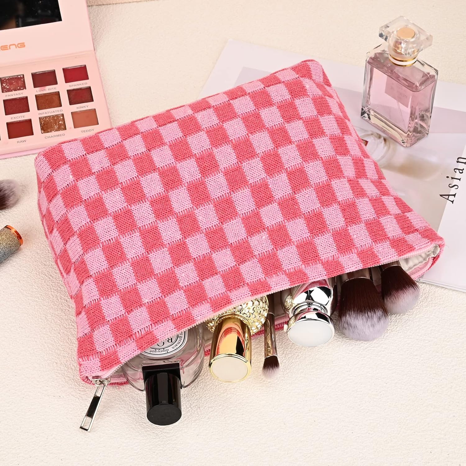 Rosa karierte Kosmetiktasche mit Make-up-Pinseln und Parfümflasche auf weißem Hintergrund.