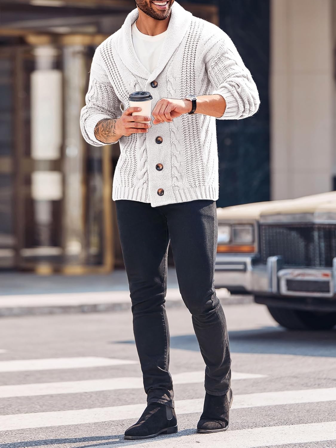 Mann in weißem Strickcardigan mit Kaffeebecher, schwarze Jeans, Straße, Herbstmode.