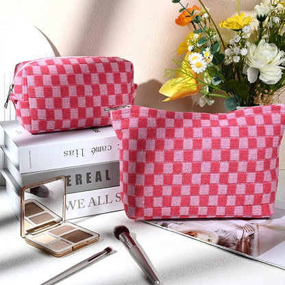 Rosa karierte Kosmetiktasche aus Stoff, neben Blumen und Make-up-Pinsel auf einem Tisch.