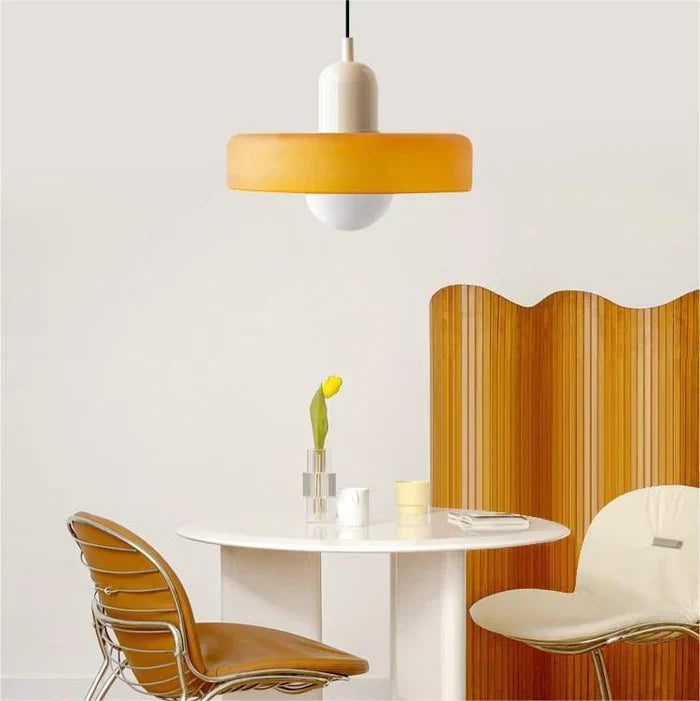 Moderne orange Hängelampe über weißem Tisch mit gelber Tulpe, braunen Stühlen und Raumteiler.