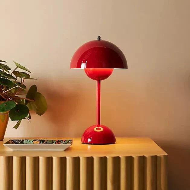 Rote Tischlampe im Retro-Stil auf Holzoberfläche neben Pflanze und Schale, Innenbeleuchtung.