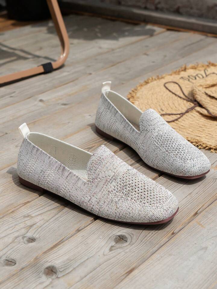 Ett par vitgrå stickade slip-on-skor med dragflik bak och brun sula på ett trägolv bredvid en halmmatta. 17
