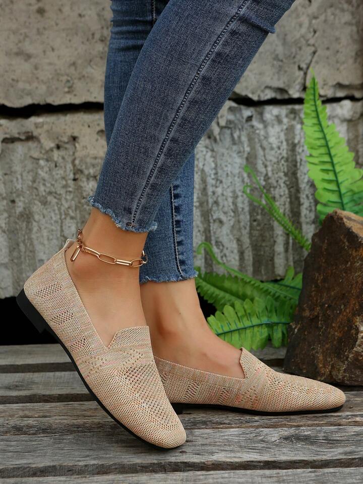Beige slip-on-skor i mesh sedda från sidan på en modell i blå jeans med guldkedja runt vristen, vid en stenvägg med ormbunkar. 4