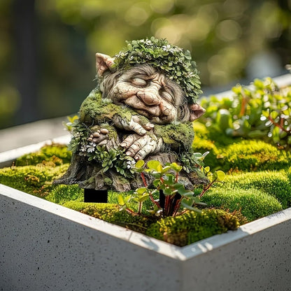 Sovande trollhuvud med bladkrans och mossa på axlarna, stående på mossa i en grå planteringslåda. 4