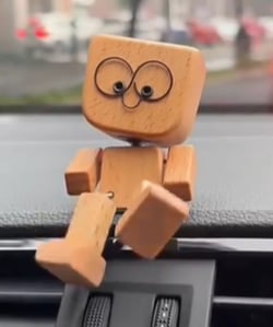 Närbild på trämannen med stora ögon på en instrumentbräda, ena benet dinglande framåt. 6