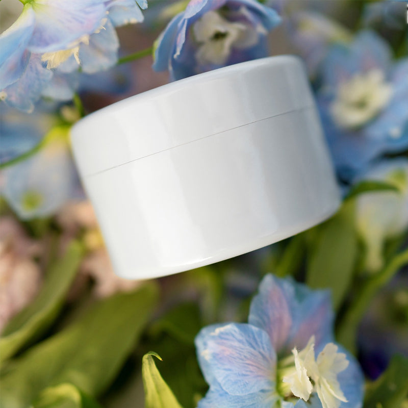 Vit rund insats sedd från sidan bland blå och vita blommor och gröna blad. 9